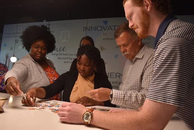 Four Rosewood team members working together on a puzzle in front of the company values wall